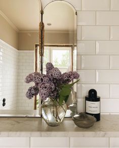 a vase filled with purple flowers sitting on top of a counter next to a mirror