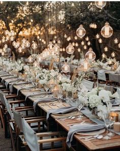 a long table with lots of lights hanging from the ceiling and flowers in vases