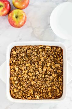 baked oatmeal in a white casserole dish next to two apples