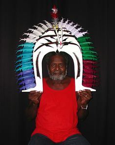 a man is holding up a paper mask with feathers on it's head and wearing a red shirt