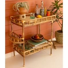 a bamboo bar cart with bottles and drinks on it next to a potted plant