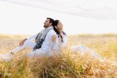 a man and woman sitting on the ground in tall grass with their arms around each other