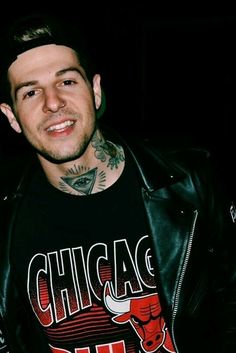 a man wearing a chicago bulls t - shirt and black leather jacket smiling at the camera