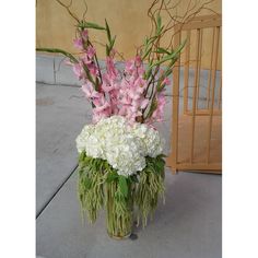 a vase filled with pink and white flowers next to a wooden cage on the sidewalk