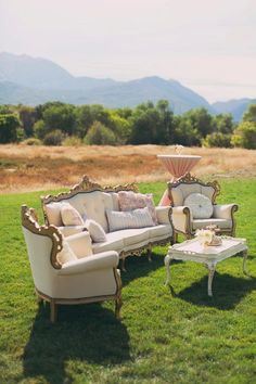 two couches and a coffee table in the middle of a grassy area with mountains in the background