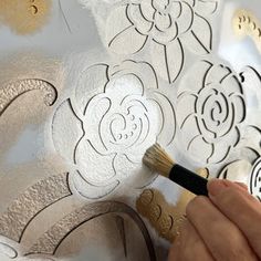 someone using a brush to paint the flowers on a wallpapered surface with gold and silver foil