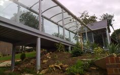 a glass and steel walkway over a hill in front of a house on a cloudy day