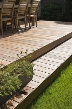 a wooden deck with chairs and plants in the grass next to an outdoor dining table