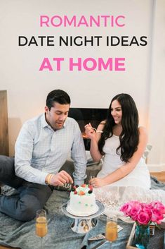 a man and woman sitting on the floor cutting into a cake with candles in front of them