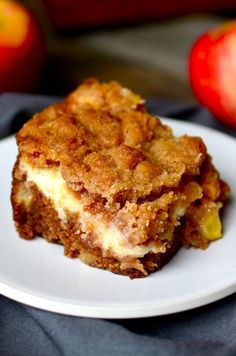 a piece of cake sitting on top of a white plate next to an orange and red apple