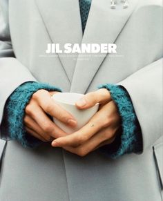 a person wearing a coat and holding a cup in their hands with the words jil sander written on it