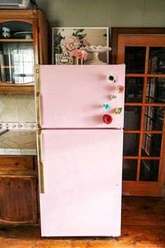 a pink refrigerator with magnets on it in a kitchen next to a wooden cabinet