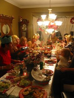 a group of people sitting around a table with food and drinks on it, all dressed in christmas hats