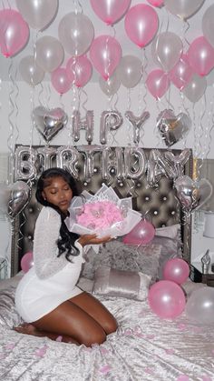 a woman sitting on top of a bed holding a bouquet of pink flowers and balloons