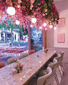 a long table with lots of chairs and flowers hanging from it's ceiling in a restaurant