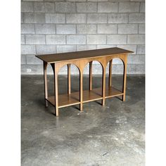 a wooden table sitting on top of a cement floor next to a brick wall in an empty room