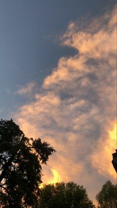 the sun is setting behind some clouds in the sky above trees and a clock tower