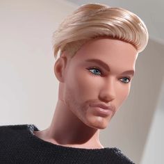 a male mannequin with blonde hair and blue eyes wearing a black sweater in front of a white wall