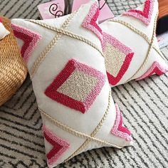 two decorative pillows sitting on top of a couch next to a wicker basket and pen