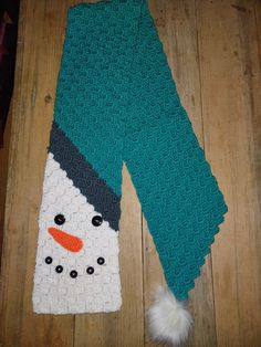 a crocheted snowman scarf laying on top of a wooden floor next to a white fur ball