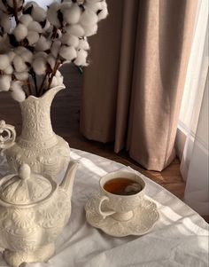 a white vase with cotton in it next to a cup and saucer