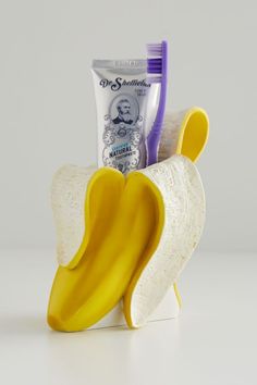 a banana shaped toothbrush holder with two toothpaste tubes in it and a tube of shaving cream on top