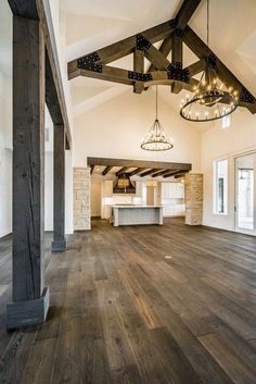 an empty living room with wood floors and exposed beams on the ceiling is lit by chandeliers