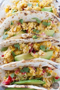 three burritos filled with eggs, avocado and cilantro