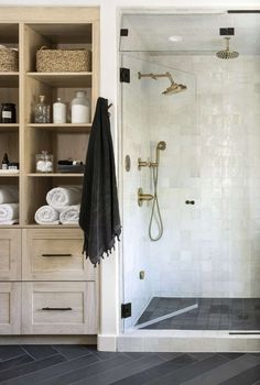 a walk in shower sitting next to a wooden shelf filled with towels and other items