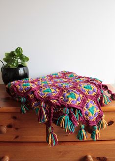 a crocheted blanket sitting on top of a wooden dresser next to a potted plant