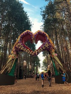 people walking under a heart shaped archway in the woods