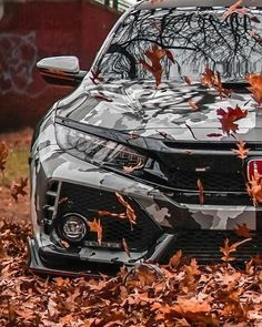 the front end of a gray car with leaves on it and trees in the background