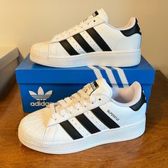 The Classic Adidas Superstar Sneaker In All White With Black 3-Stripes, Black Heel Tab With White Trefoil Logo, And Black Superstar On Sides. Lace Closure, Shell Toe, Sturdy And Comfortable. The Xlg Has A Slightly Elevated Midsole. Cute Sneaker! Nwt Mint Condition, Comes In Original Adidas Box. Sold Out On Line. Qt8f4x5d4a4tt Superstar Adidas, Black Superstar, Adidas Shoes Superstar, Classic Adidas, Adidas Shoes Women, Adidas Original, Cute Sneakers, Black Heel, Shoes Adidas