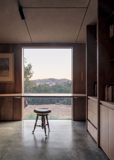 an empty room with a stool and large window looking out onto the countryside outside at dusk