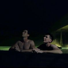 two men are sitting in the water at night, one is looking up to the sky