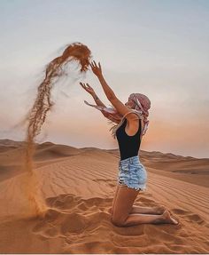 a woman sitting on top of a sandy beach next to a brown sand dune and throwing it in the air