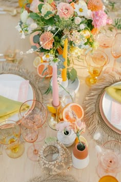 the table is set with pink and yellow flowers in vases, candles, plates, and napkins