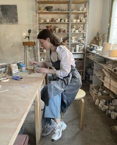 a woman sitting at a table working on pottery