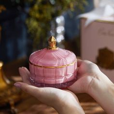 a woman's hand holding a pink glass jar with a gold decoration on top