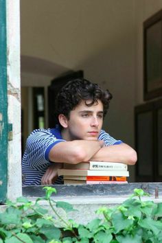 a young man leaning his head on top of two books while looking out the window