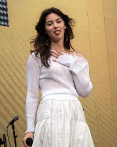 a woman standing in front of a microphone and wearing a white dress with long sleeves