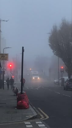 foggy street with cars and people walking on the side walk in front of traffic lights