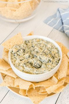 a white bowl filled with spinach dip surrounded by tortilla chips