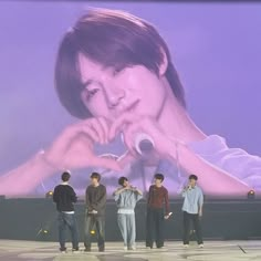 four young men standing on stage in front of a large screen with an image of a woman