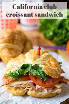 a sandwich with meat, lettuce and tomato sitting on wax paper next to some croissants