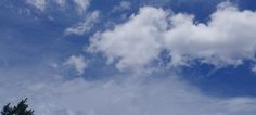 the sky is filled with white clouds and some green trees in front of blue skies