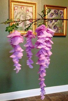 purple flowers are hanging from a branch in front of two paintings