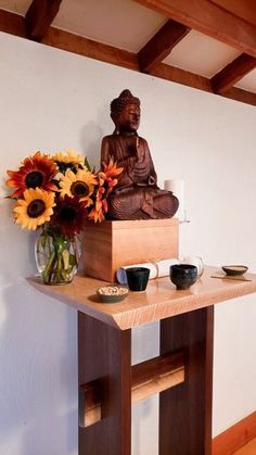 a buddha statue sitting on top of a wooden table next to a vase filled with flowers