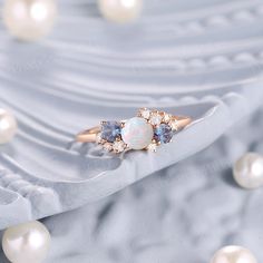 an opal and diamond ring sits on top of pearles in front of a white background