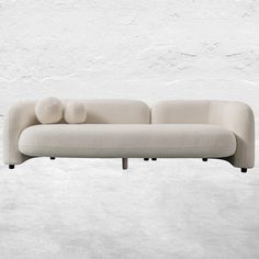 a white couch sitting on top of a cement floor next to a wall with two pillows